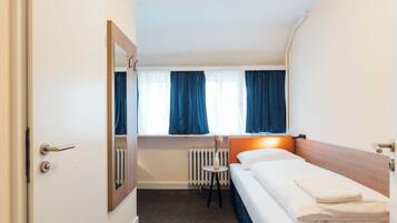 Ein Hotelzimmer mit Bett, einem kleinen Tisch mit Vase, einem Fenster mit Vorhängen und einer Heizung.