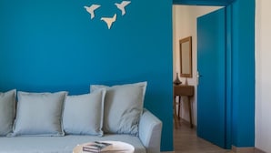 A room with a blue wall, a grey sofa, a small round table with a book, and a door leading to another room. - Anemi Blue apt-close to the beach (Rethymno)