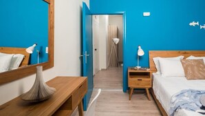 A hotel room with a wooden bed, a bedside table, a mirror, and a blue accent wall. - Anemi Blue apt-close to the beach (Rethymno)