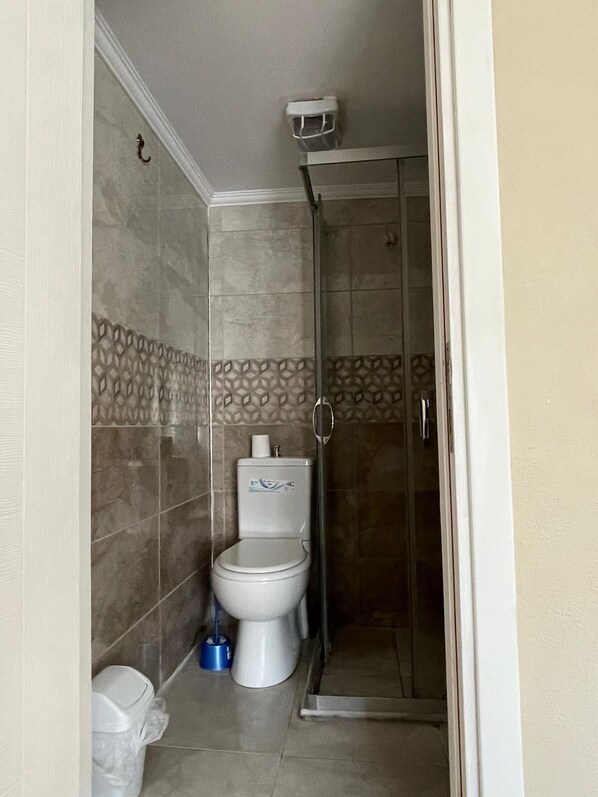 Un baño con inodoro, ducha y cubo de basura.