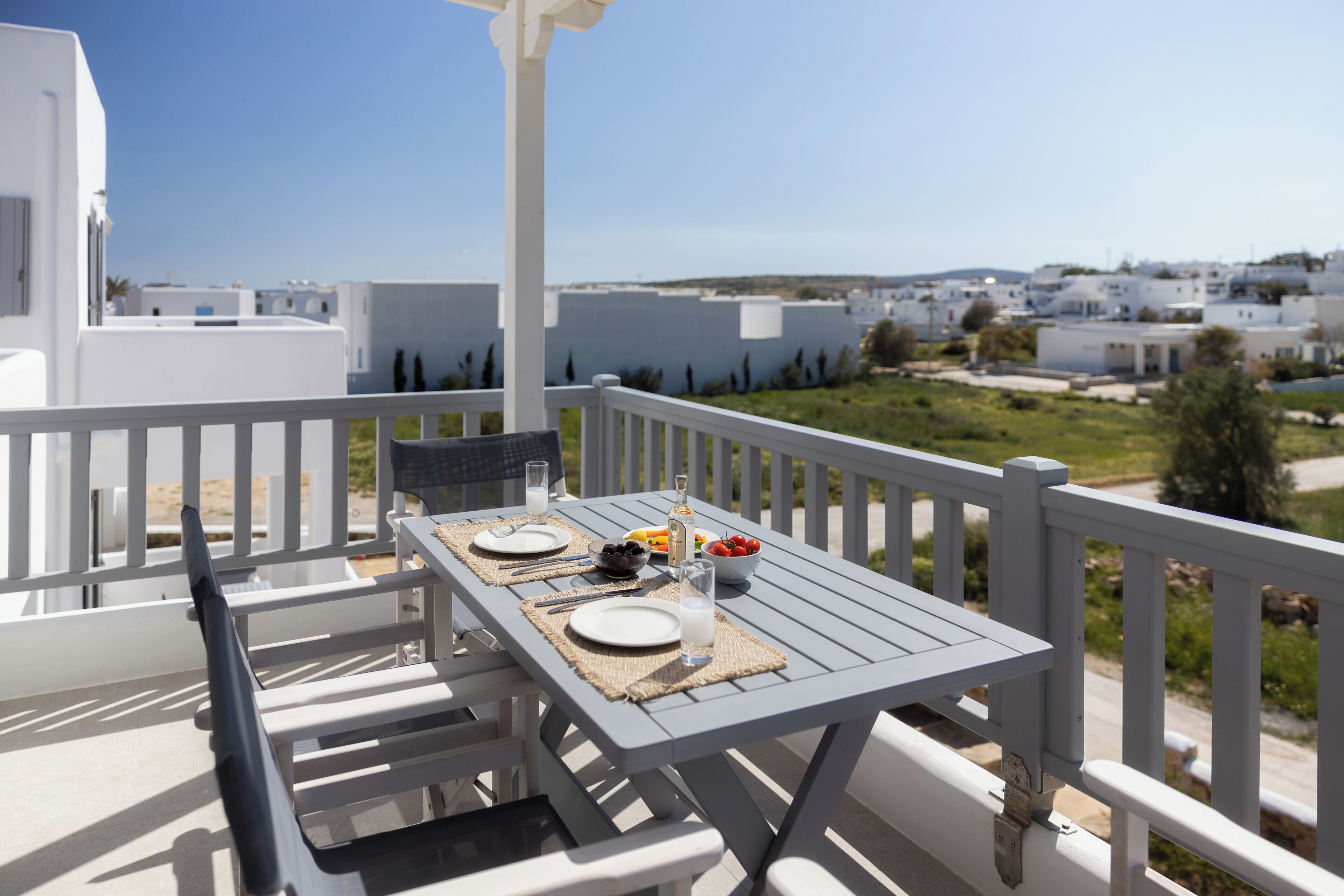 A balcony with a table set for two, overlooking a coastal village.