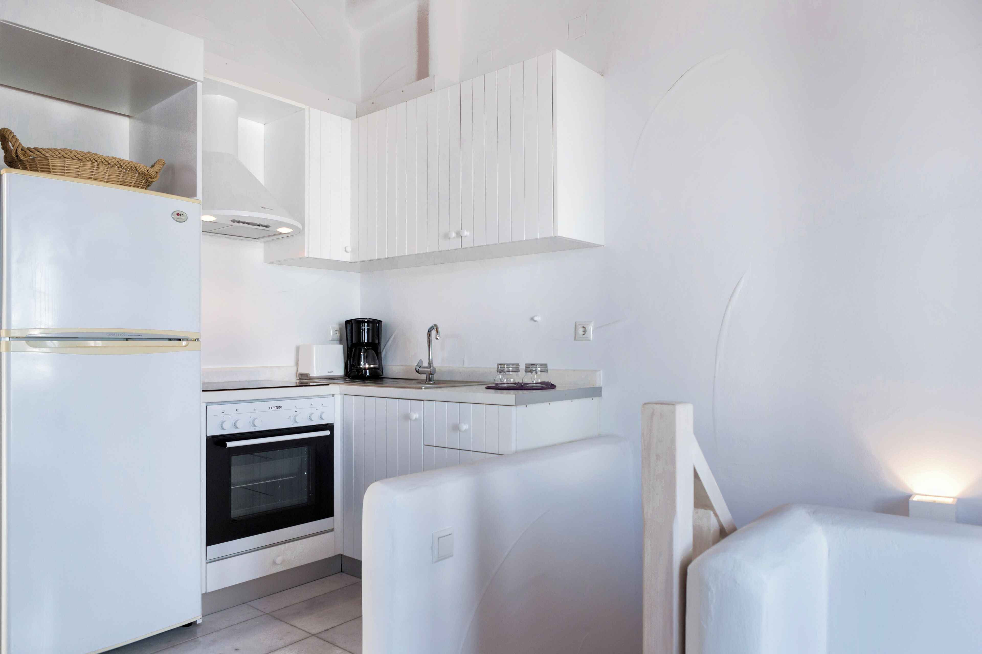 A modern kitchen with white cabinetry, a built-in oven, a coffee maker, and a basket on the refrigerator.