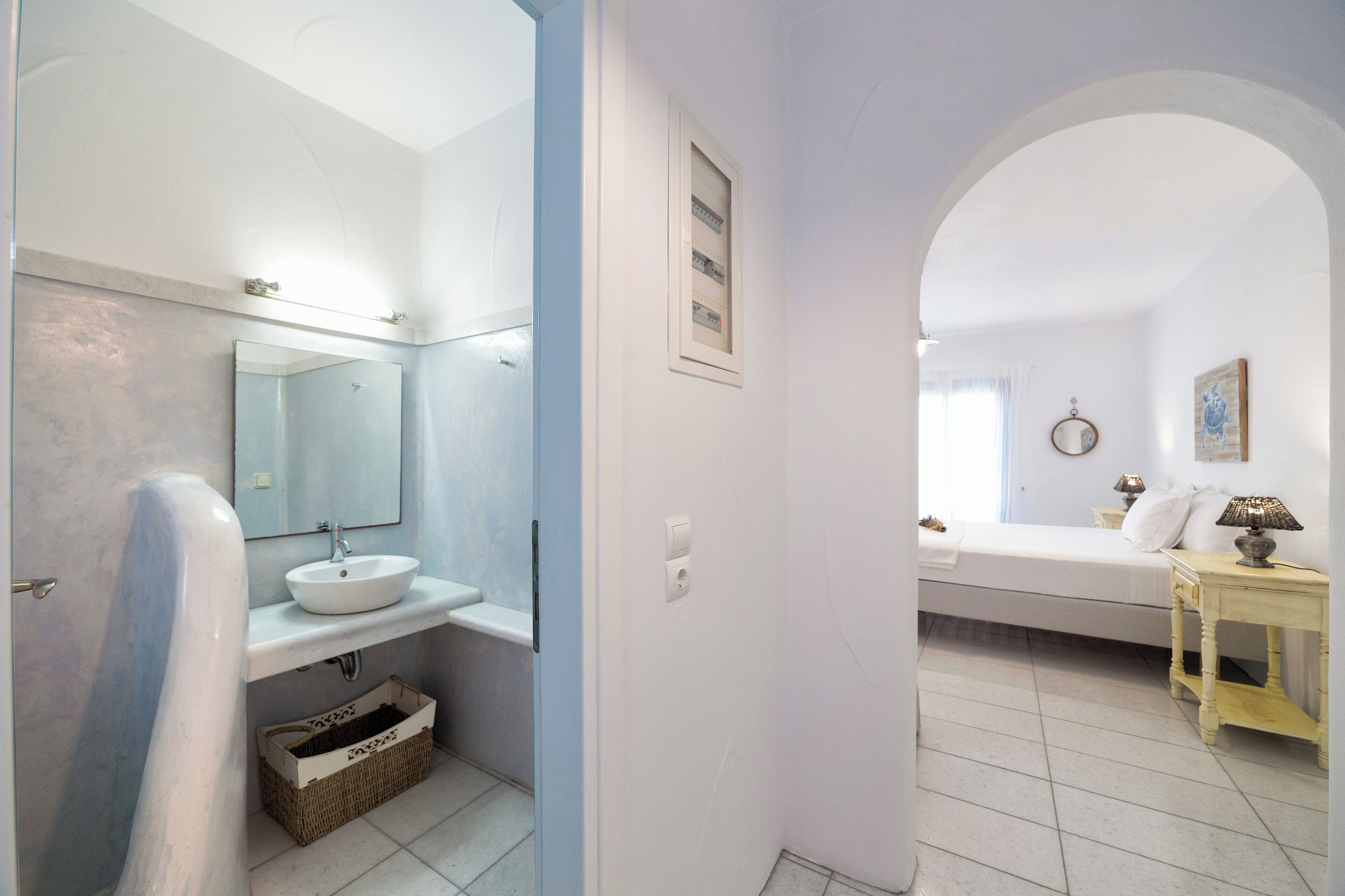 A bathroom with a bathtub, a sink, and a mirror. There is a basket under the sink and a towel hanging on the wall.