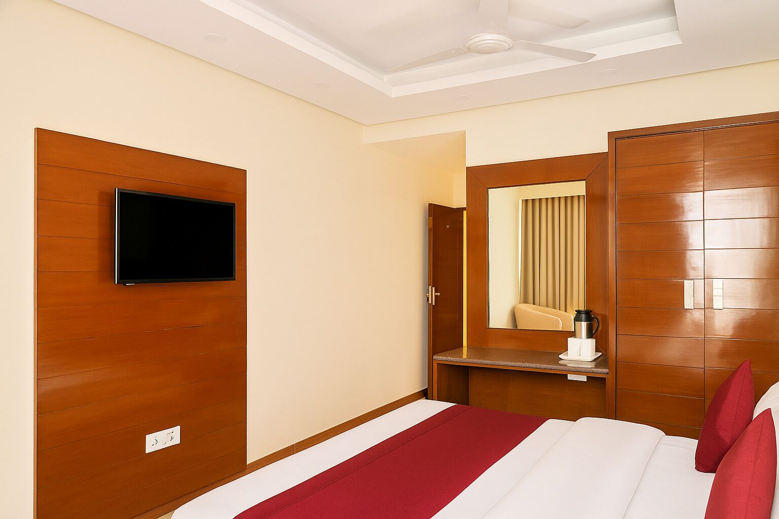 A hotel room with a bed, a TV mounted on the wall, a mirror, and a wardrobe.