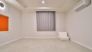 A room with a carpeted floor, a window with curtains, a white chair, and an air conditioning unit. - Hotel Dongnae (Busan)