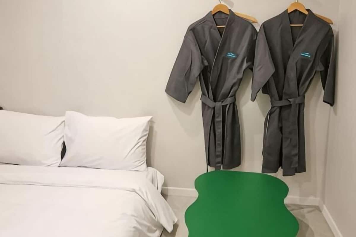 Hotellihuone, jossa on sänky, seinälle ripustettuina kaksi kylpytakia ja vihreä tuoli.