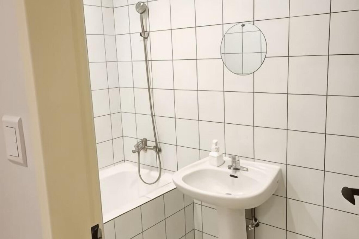 A bathroom with white tiles, a white sink, and a shower.