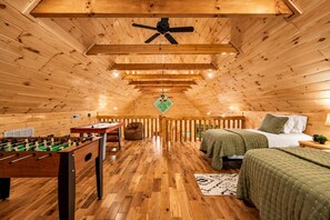 Une pièce chaleureuse avec un plafond en bois, un lit, un futon, une table de baby-foot et un fauteuil en forme de sac de haricots.