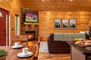 L’intérieur chaleureux d’un chalet avec une cheminée, des murs en bois, un téléviseur et un coin repas avec une table mise pour deux personnes.