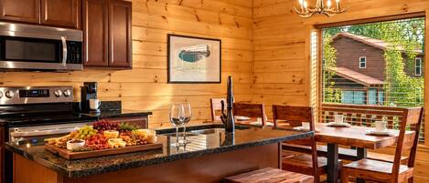 A wooden cabin interior with a kitchen, dining area, and a view of a house through a window.