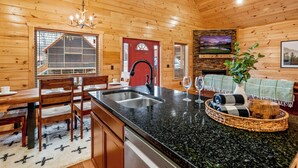 L’intérieur d’un chalet en bois comprend un coin cuisine doté d’un plan de travail en granit, une table à manger avec des chaises, une porte rouge et une cheminée.