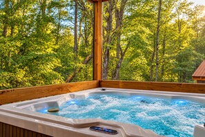 A hot tub with a wooden deck and a view of a forest.