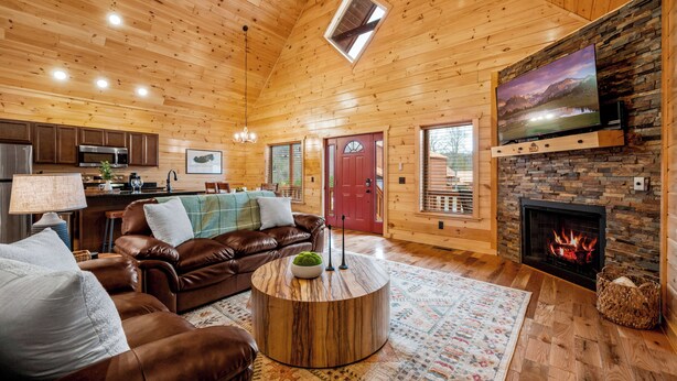 L’intérieur d’un chalet confortable, avec une cheminée, un téléviseur fixé à un mur en pierre, un canapé en cuir et une table basse ronde.