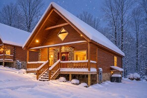 Une cabane en bois dotée d’un porche et d’un escalier, entourée d’arbres couverts de neige.