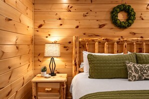 A wooden cabin room with a bed, a nightstand with a lamp, and a wall-mounted wreath.