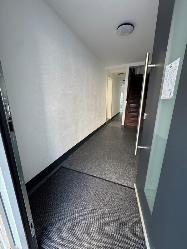 Un pasillo con piso alfombrado, una puerta a la derecha y una escalera al fondo.