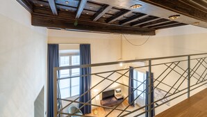 Un interior moderno con techo de madera, una escalera con barandilla de metal y una habitación con televisor y escritorio.