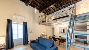 Una sala moderna con un sofá azul, suelo de madera, una escalera y un comedor.