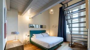 Un dormitorio moderno con cama, mesita de noche, lámpara, obra de arte y ventana con cortinas.