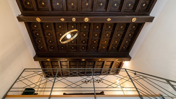 Un techo alto con paneles de madera ornamentados y una lámpara circular central.