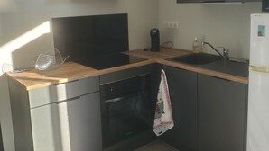 Una cucina moderna con mobili scuri, un piano di lavoro in legno, una cappa aspirante nera, un forno a incasso e un frigorifero bianco.