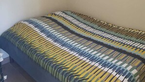 Un letto singolo con una coperta a motivi in una stanza con una finestra e una porta.