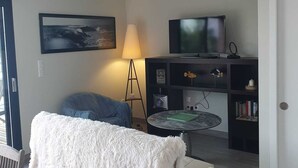 Un soggiorno con un divano, una televisione, una lampada e una libreria.