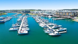 A marina with numerous boats docked, a modern building complex, and a clear blue sky.