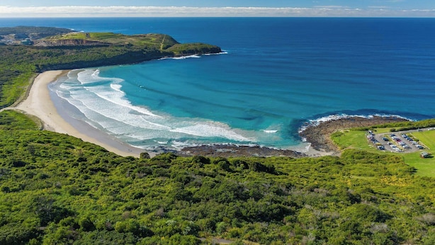 An aerial view of a coastal area with a beach, parking lot, and lush greenery.
