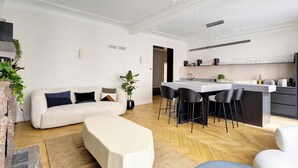 Un salon moderne avec un canapé, une table basse et un coin repas comprenant des chaises, et une cuisine en arrière-plan.