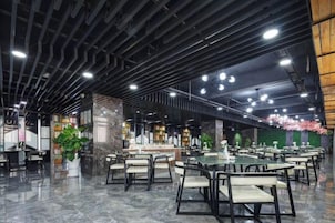 A spacious indoor area with multiple tables and chairs, a central bar area, and decorative plants.