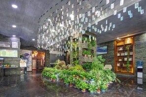 A lobby with a reception desk, a plant display, and a wall with hanging notes. - Aoshang Hotel (Hanzhong High-speed Railway Station) (Hanzhong)