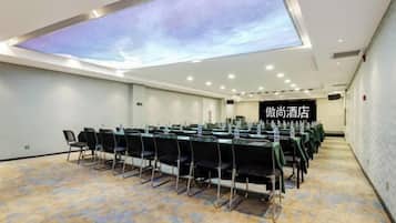 Un salón de conferencias con proyección de cielo estrellado en el techo, una larga mesa con sillas y un cartel que indica la ubicación de un hotel.