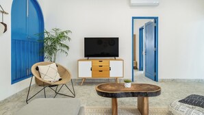 A room with a blue door, a television on a wooden cabinet, a wicker chair, a round wooden table, and a potted plant. - Casa Posa Seminyak (Seminyak)