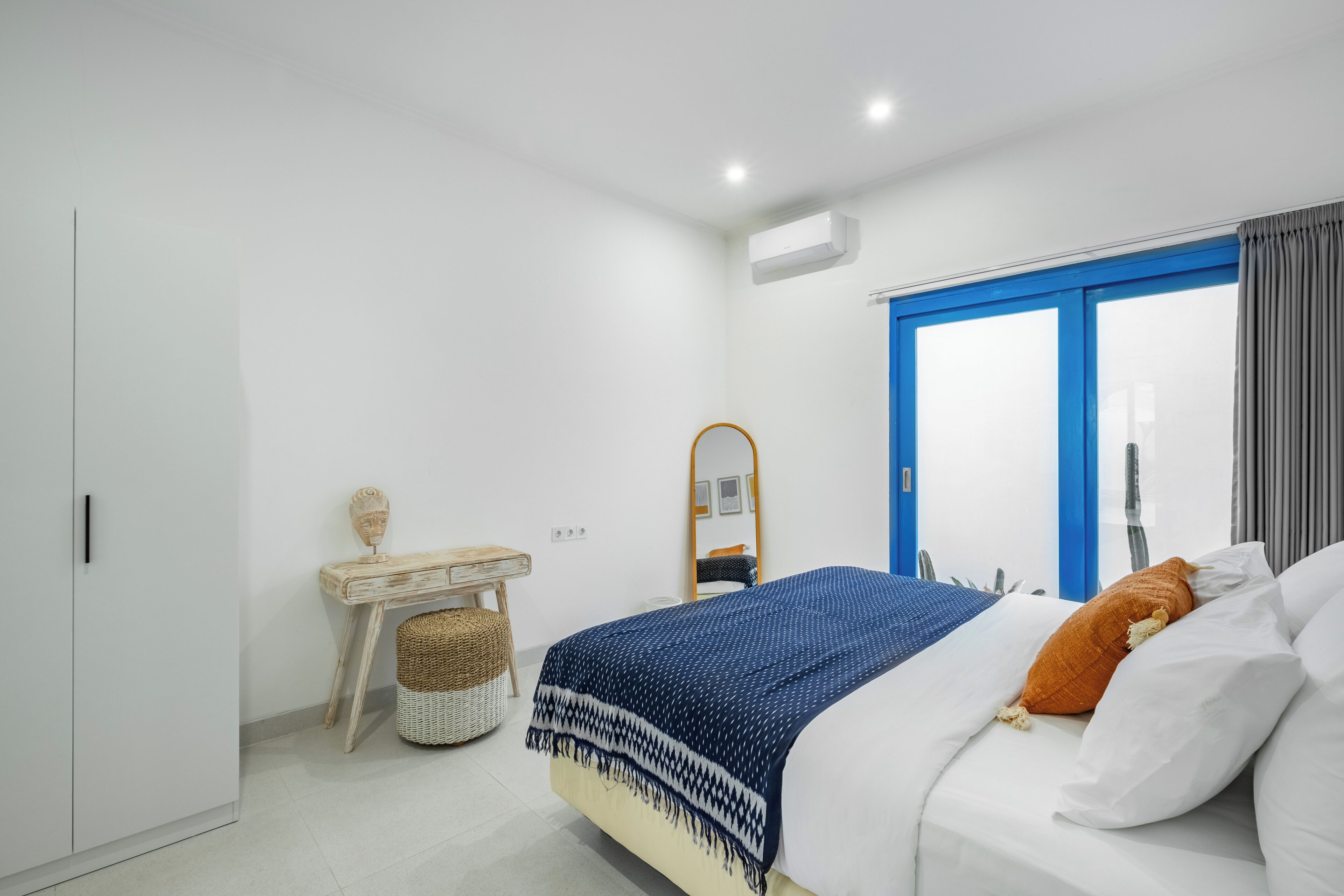 A bedroom with a bed, a bedside table, a mirror, and a window with curtains.