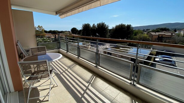 A balcony with a table and chairs, a view of a road and parked cars, and a clear sky.