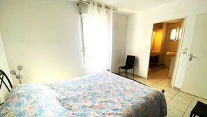 A bedroom with a floral bedspread, a chair, and a view into a bathroom.