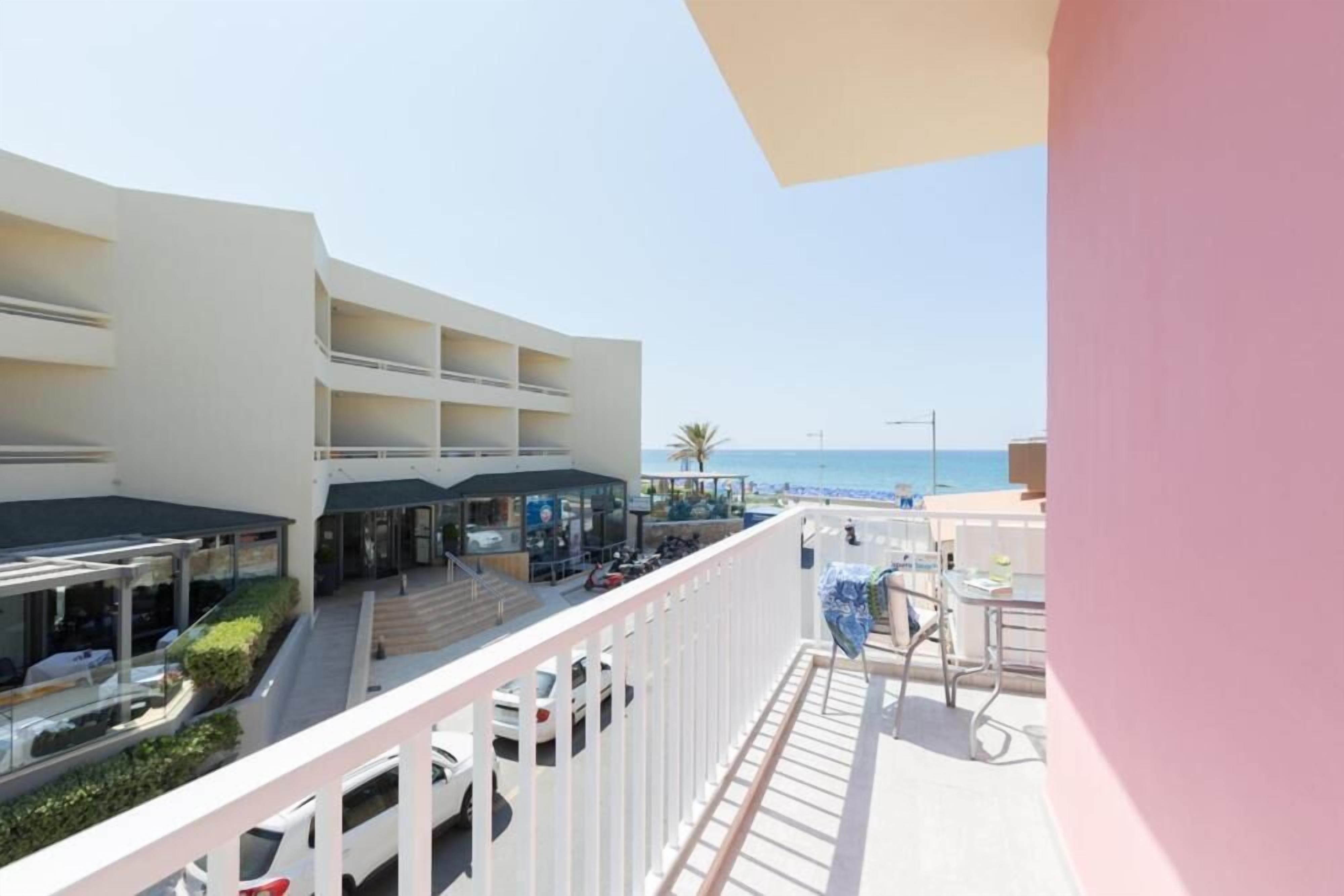 A hotel with multiple balconies overlooking a beach. There are several outdoor seating areas and a pool.