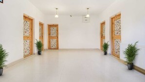 Un pasillo amplio y luminoso con suelo de baldosas, puertas de madera ornamentadas y plantas en macetas.