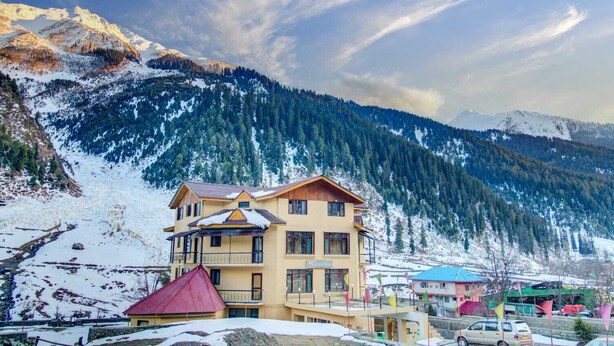 Un hotel de varios pisos con balcones, con vistas a montañas nevadas y cielos despejados.