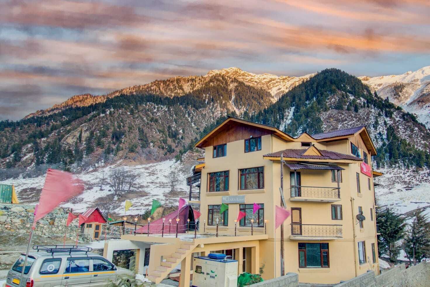 A multi-story building with balconies, a sign indicating a restaurant, and a mountainous backdrop.