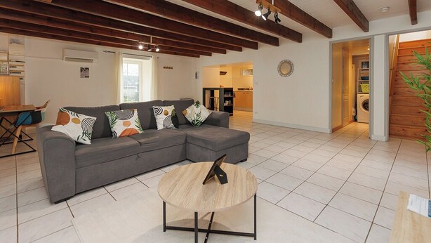 A modern living room with a grey sectional sofa, a round wooden coffee table, and exposed wooden beams on the ceiling. - LE SOUVENIR D'AILLEURS T2 65m² near Futuroscope (Lhommaizé)