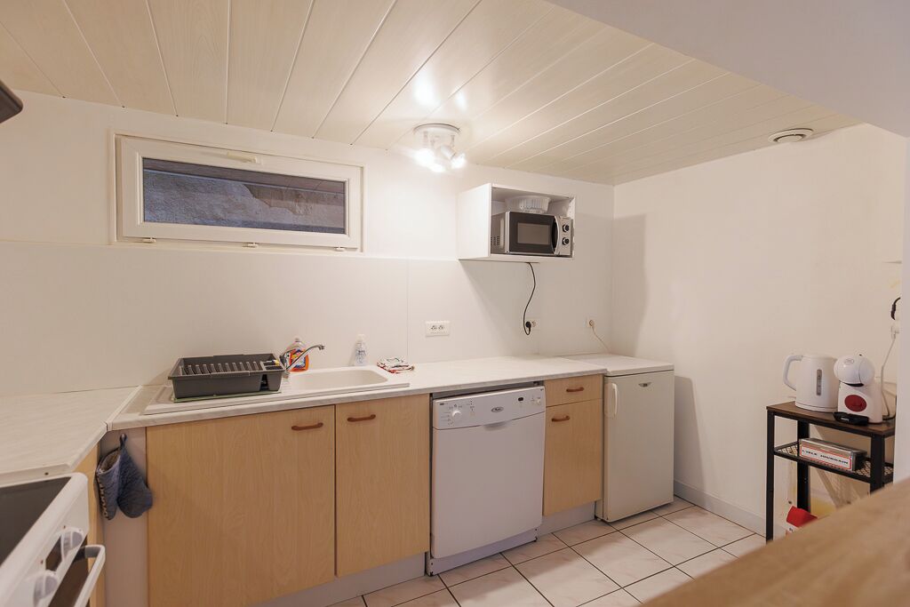 A compact kitchen with wooden cabinets, a dishwasher, a microwave, and a small shelf with a kettle and a coffee maker.