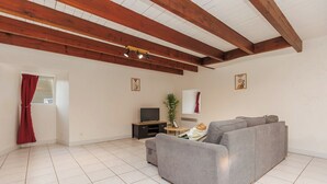 A living room with a grey sofa, a flat-screen TV, and wooden beams on the ceiling. - LE SOUVENIR D'AILLEURS T2 65m² near Futuroscope (Lhommaizé)