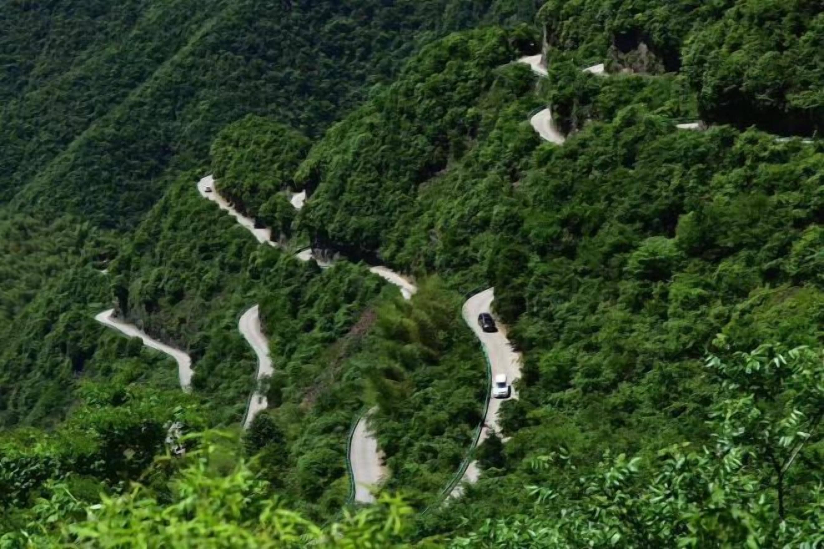 A winding mountain road surrounded by dense green forest.