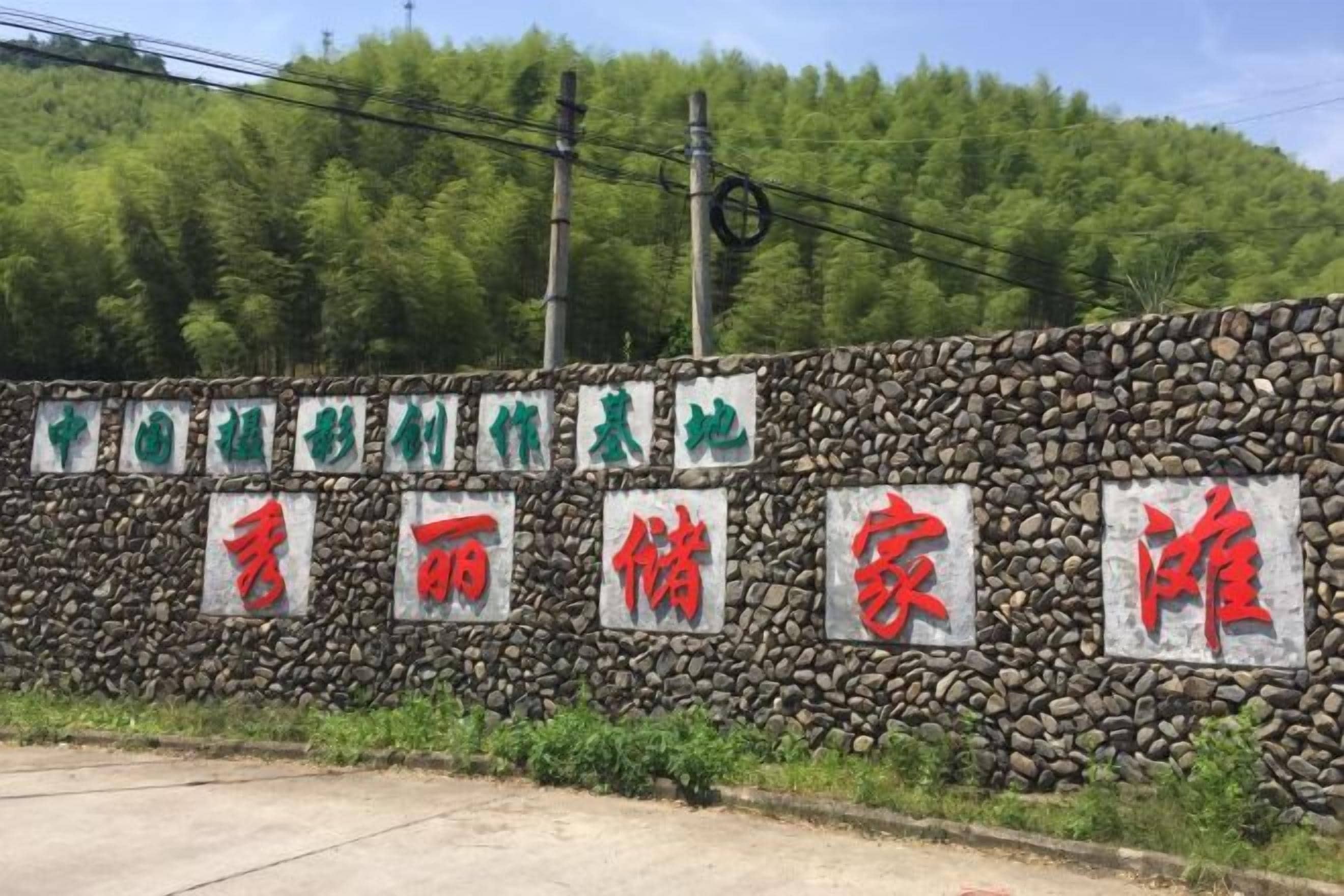 Un muro de piedra con varios carteles, algunos con texto verde y rojo, y un fondo de árboles verdes y frondosos.