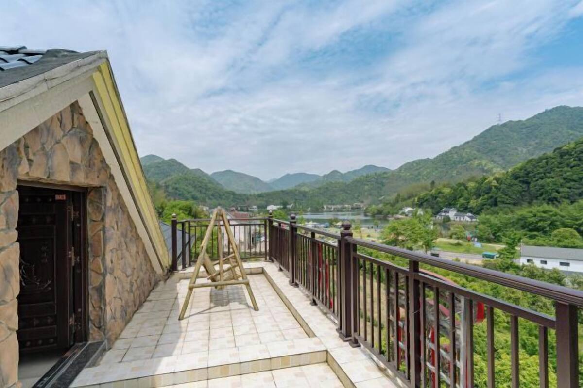 Een balkon met een stenen muur, een schommel en uitzicht op een vallei met huizen en groen.