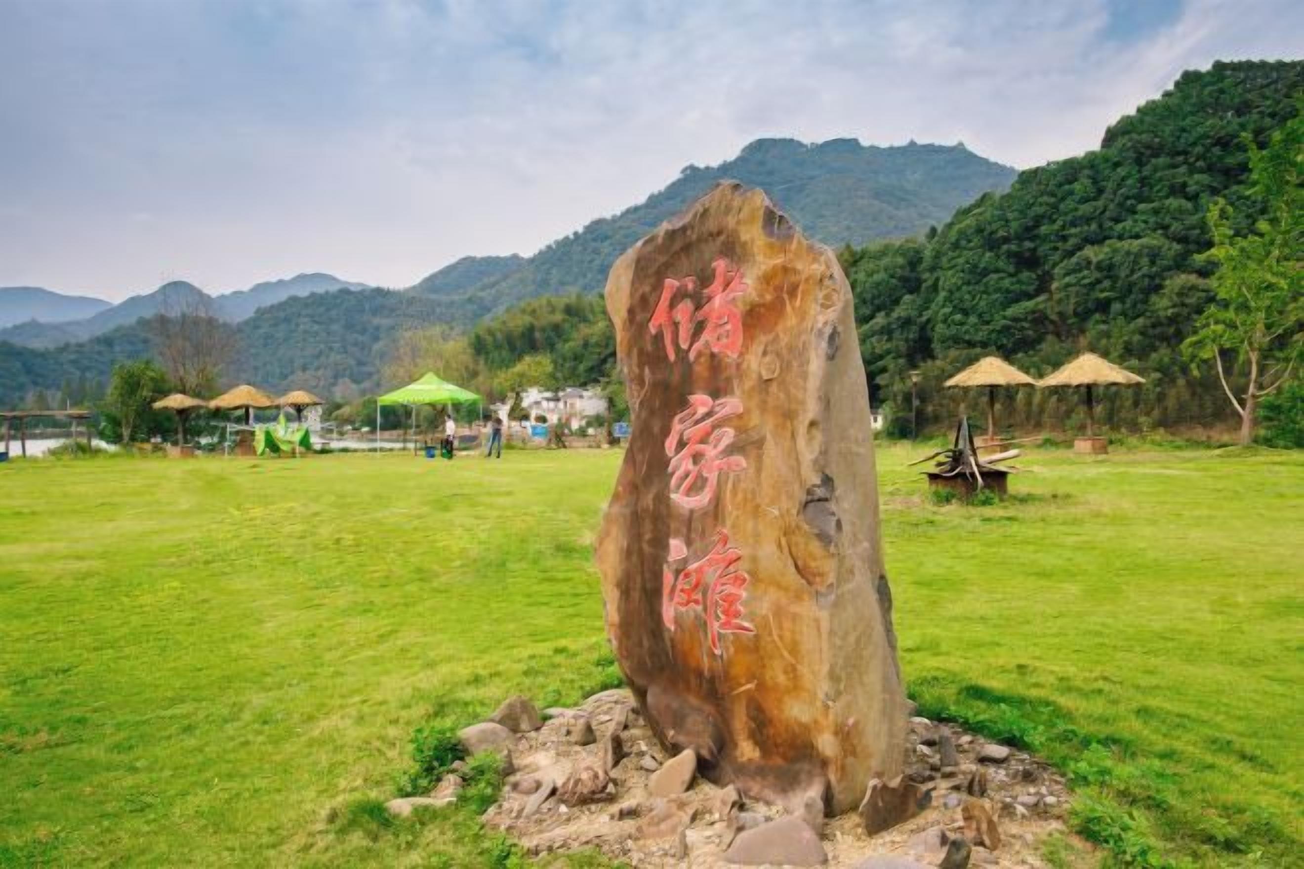 A large rock with Chinese characters in a grassy field with mountains in the background.