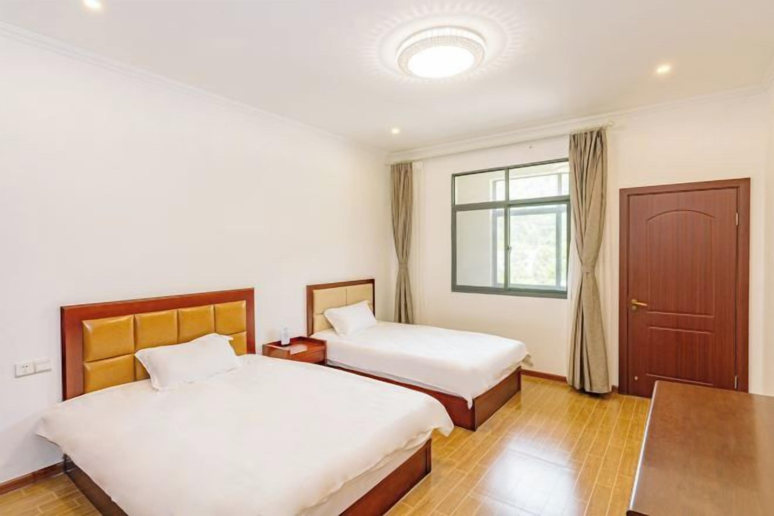 Habitación de hotel con dos camas, suelo de madera, ventana con cortinas y una puerta.
