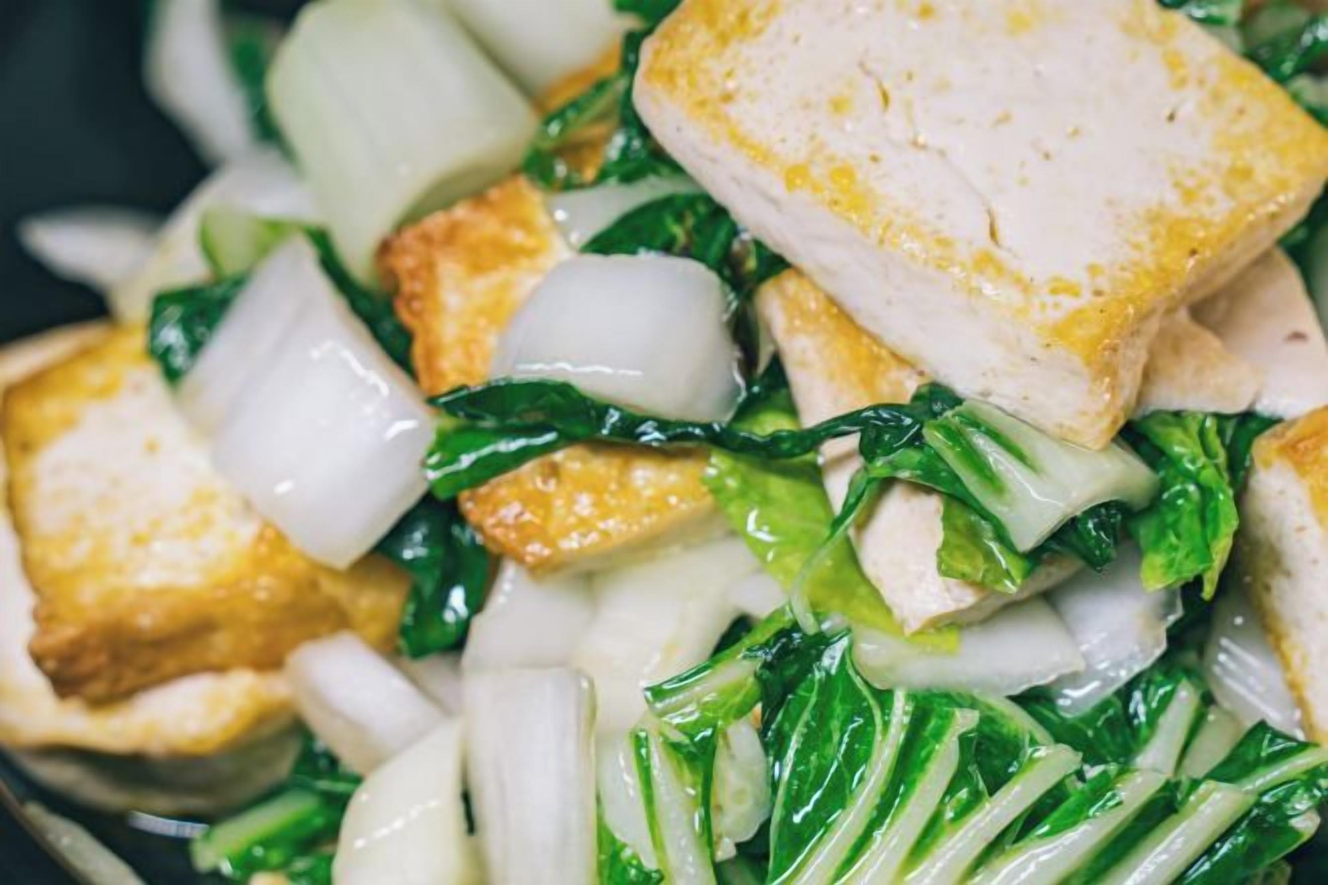 Primer plano de un plato con tofu, bok choy y cebollas blancas.